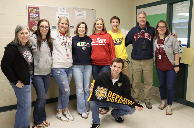 Teachers at Glacier Creek Middle School pose and smile for photo while wearing clothing related to their previous colleges