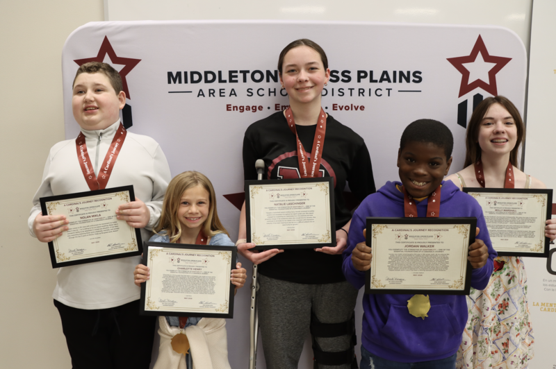 Nolan Mikla, Charlotte Henry, Natalie Laschinger, Jordan Walker, and Molly Marshall standing in front of a photo backdrop and smiling while holding their Cardinal's Journey Awards