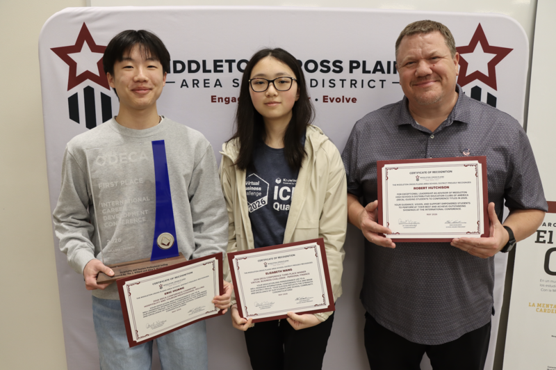 Eric Huang, Elizabeth Wang, and Robert Hutchison smiling in front of photo backdrop and holding certificates and awards
