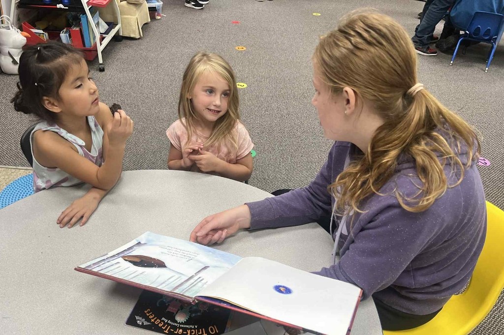 a girl reading to 2 kids