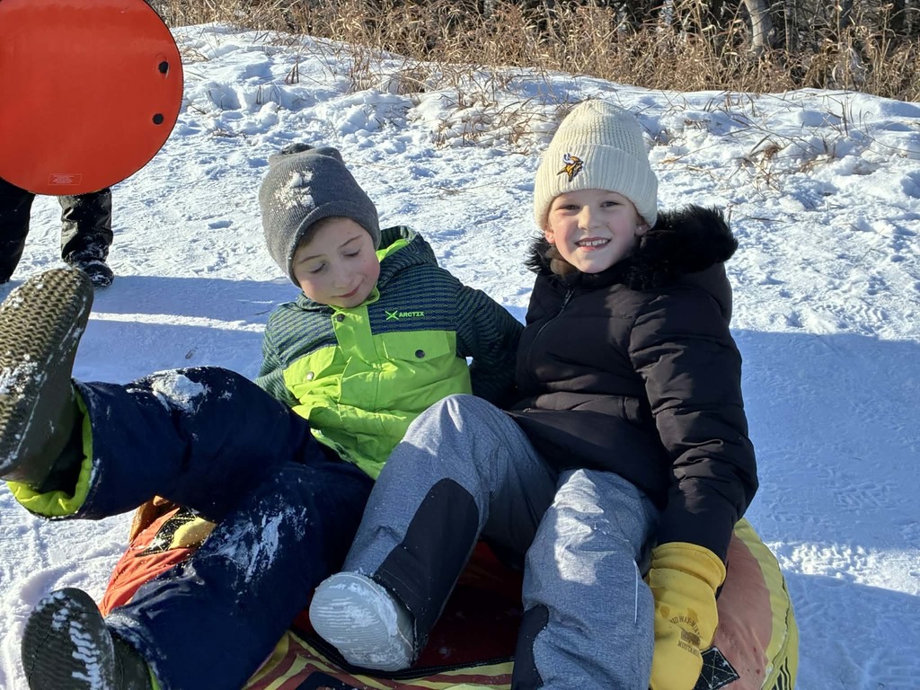 2 kids going down the hill in a tube.