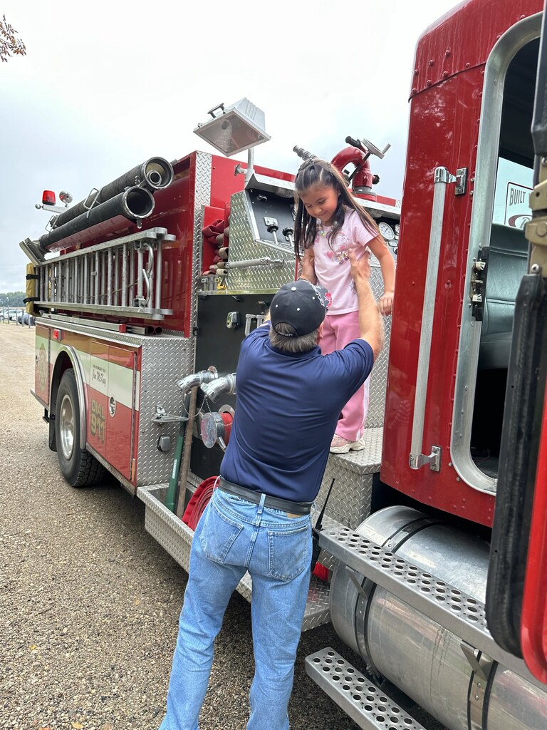 a firefighter helping a girl out of the fire truck.