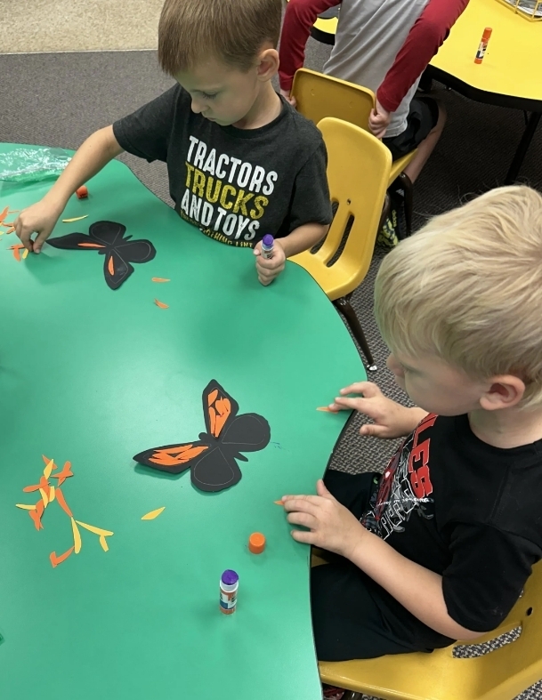 2 boys gluing paper on their butterflies 