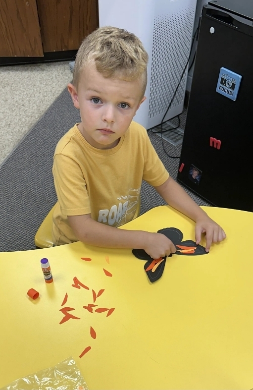 a boy gluing paper on his butterfly 