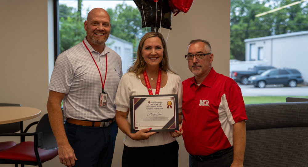 A tall man with a beard next to a woman holding a certificate next to a shorter man with glasses in a red polo