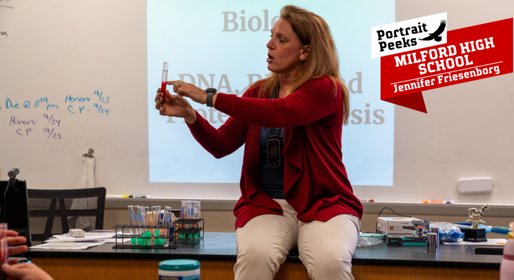 Woman in a red shaw on a lab desk holding a small vial with red and green in it