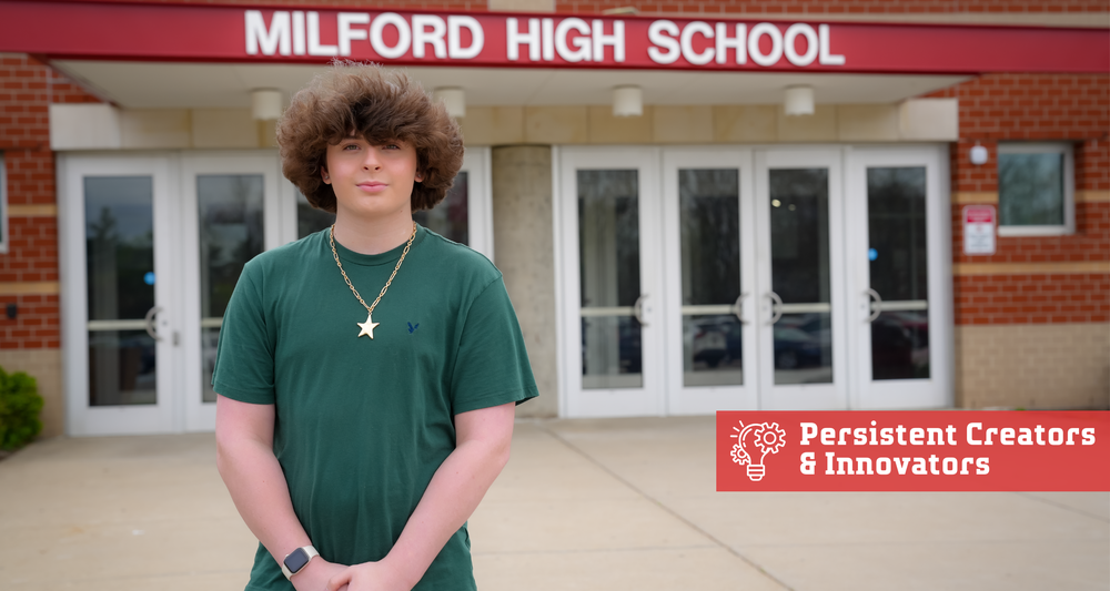 A Milford High School student stands in front of the school entrance beneath a “Milford High School” sign, wearing a green shirt and a necklace, with a graphic reading “Persistent Creators & Innovators” displayed on the image.