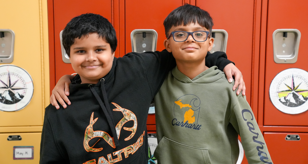 Two boys with their arms around each other standing in front of lockers