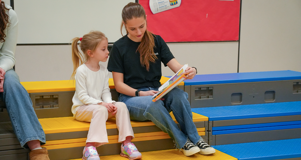 A girl in a black shirt reading to a younger girl