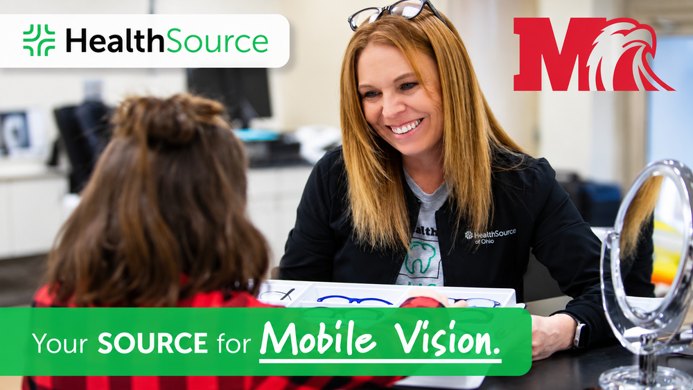 A HealthSource of Ohio representative smiles while helping a student select eyeglass frames from a display tray. The graphic features the HealthSource and Milford Schools logos and the message, “Your SOURCE for Mobile Vision.”
