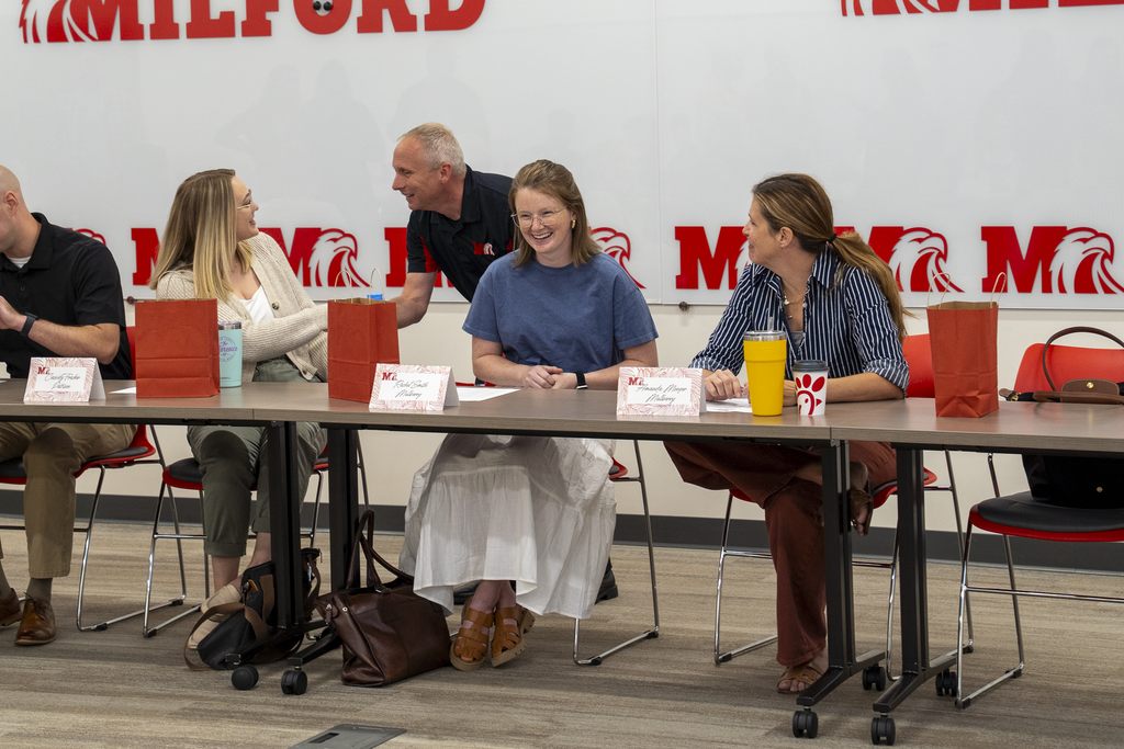 Man talking to woman next to two other smiling women at a desk