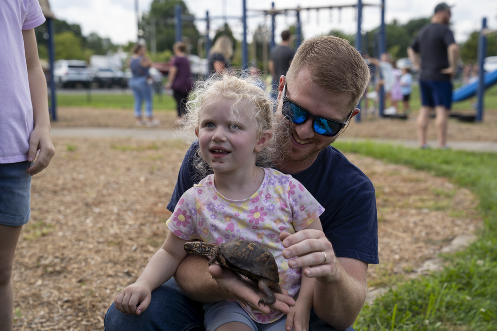 Girls holding turtle smiling with father holding her in his arms