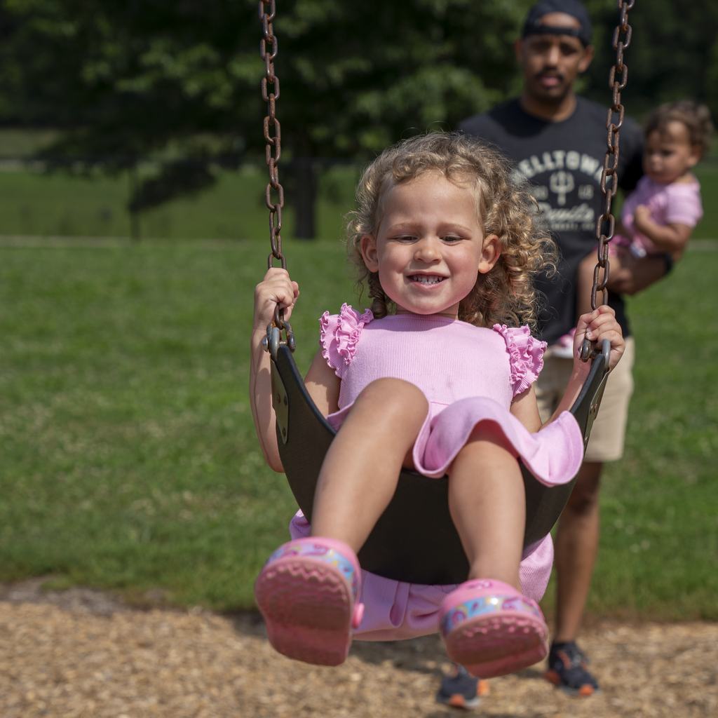 Girl in pink dress and shoes smiling on a swing