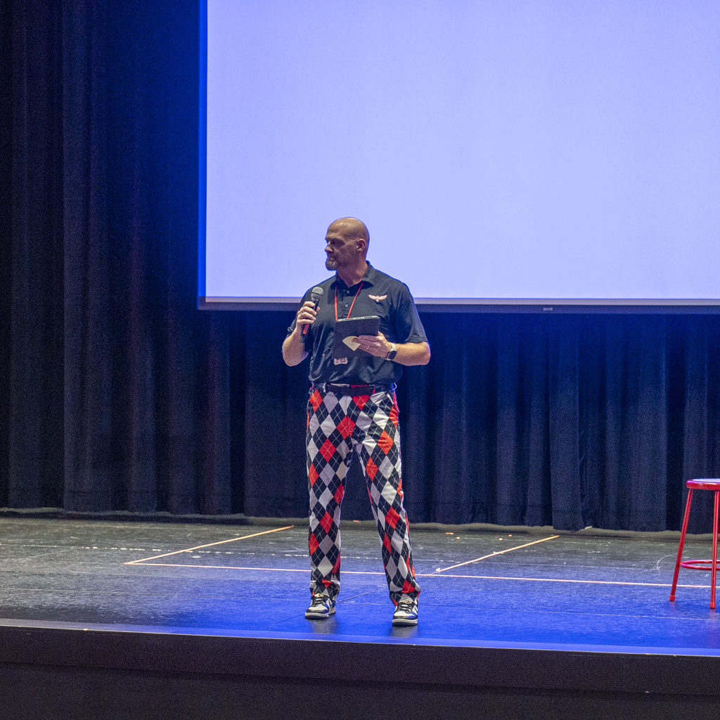 Man in red and black plaid pants with a microphone on a stage