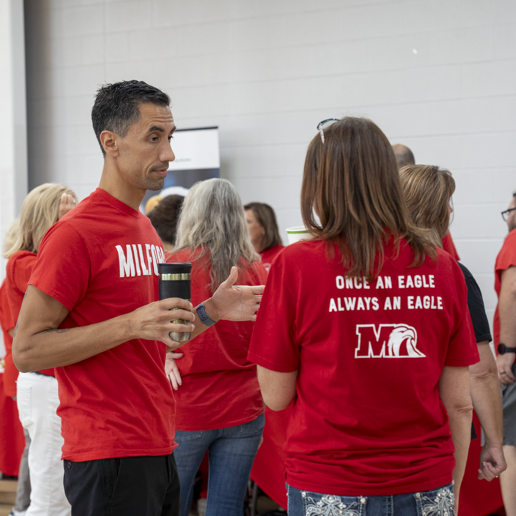 Man holding a to-go mug talking to a woman in red