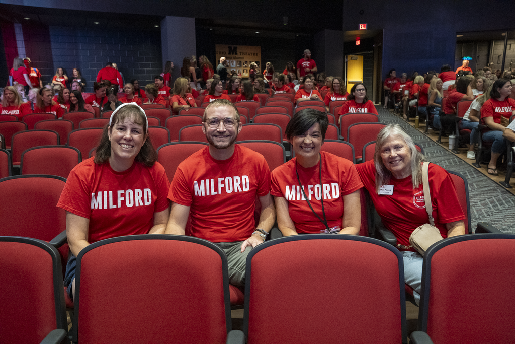4 people sitting down in red milford shirts smiling at the camera