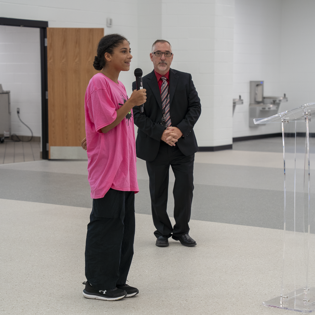 girl in pink web shirt smiling while holding a microphone