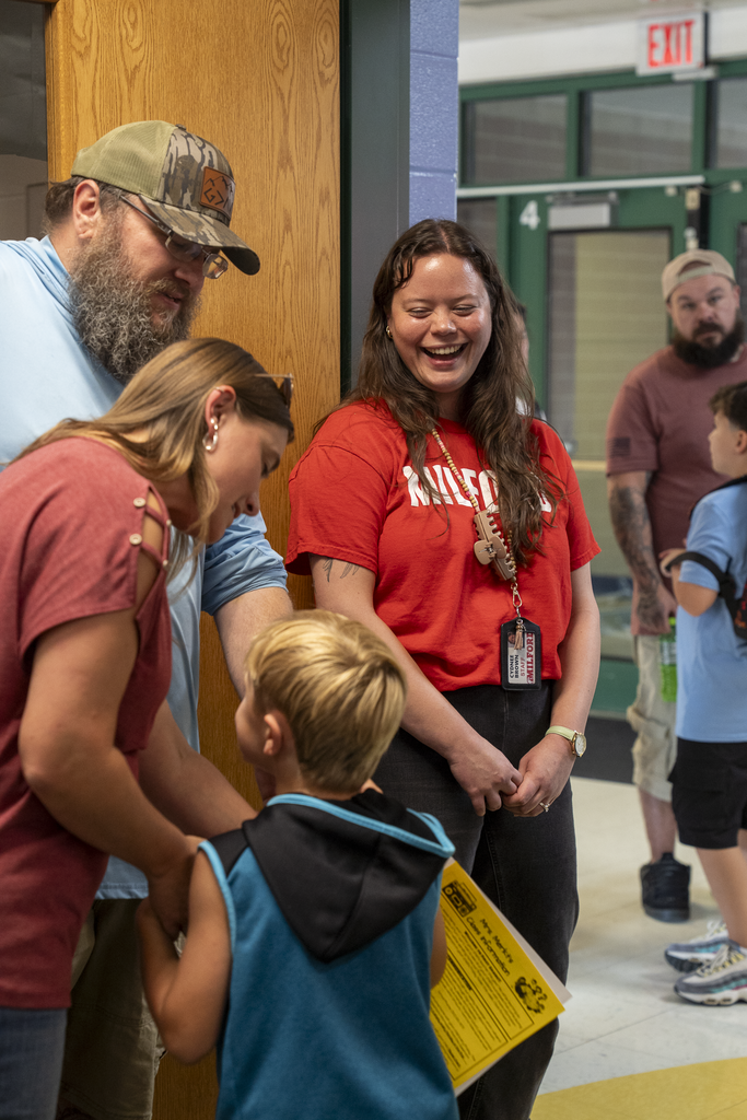 young brown haired teacher in red shirt laughing with parents and student