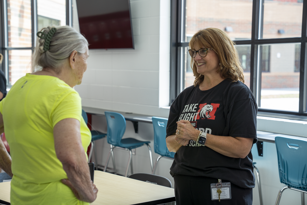 Female teacher with glasses smiling at woman in bright green shirt