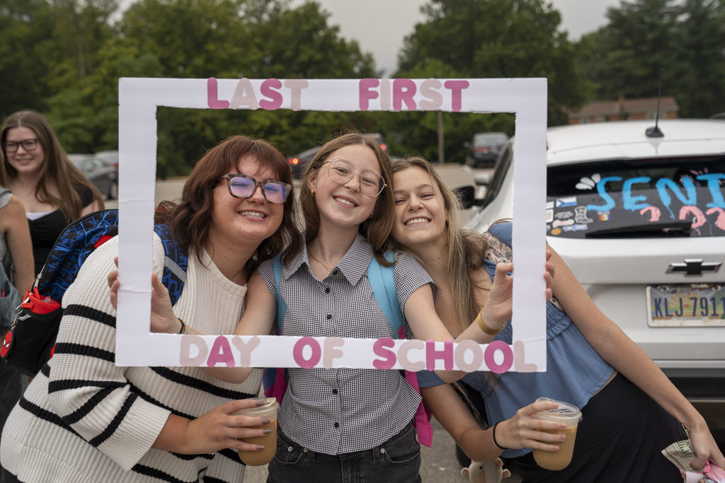 three girls holding a "last first day of school" frame over their faces