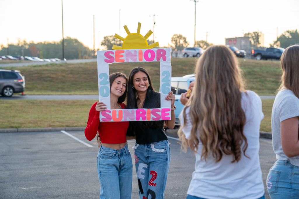 Two girls standing in a prop frame with the words "senior sunrise"