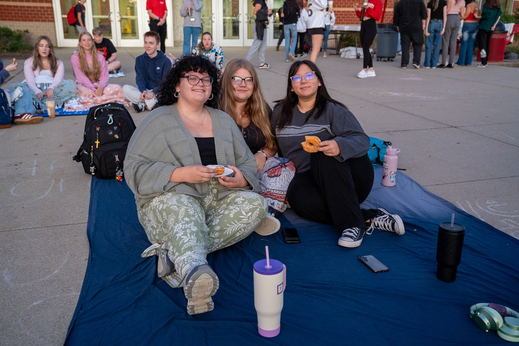 Three girls lying on a blanket on the concrete in front of a high school
