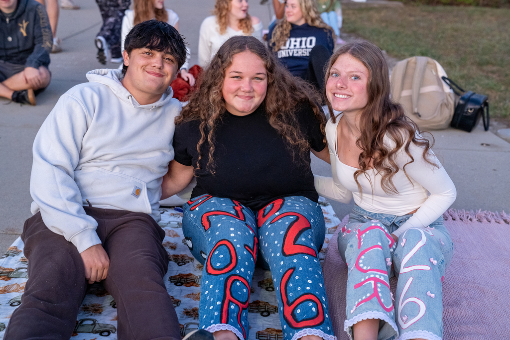 Three teenagers laying down on the concrete with blankets and jeans saying "senior 2026"