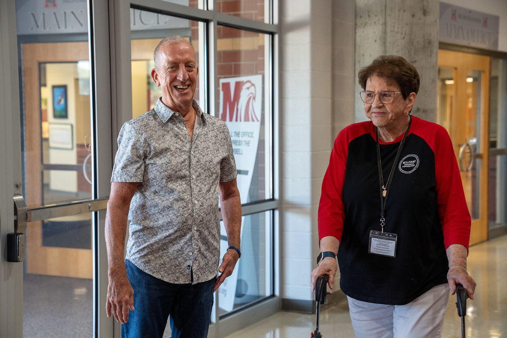 Older man in button down shirt smiling at the camera next to a woman in glasses 