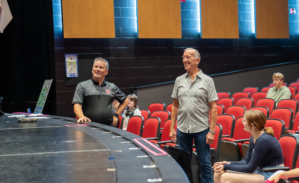 Man with polo next to stage smiling next to a man in a button down shirt