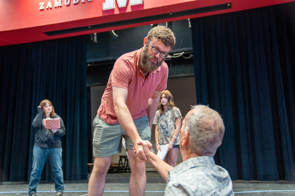 Man in a polo giving a handshake to an older man beneath him and the stage