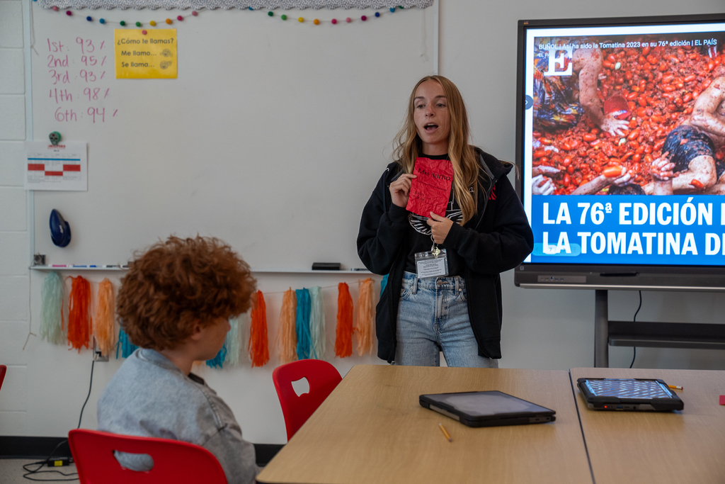 blonde hair female teacher holding red piece of paper talking to a boy with red hair
