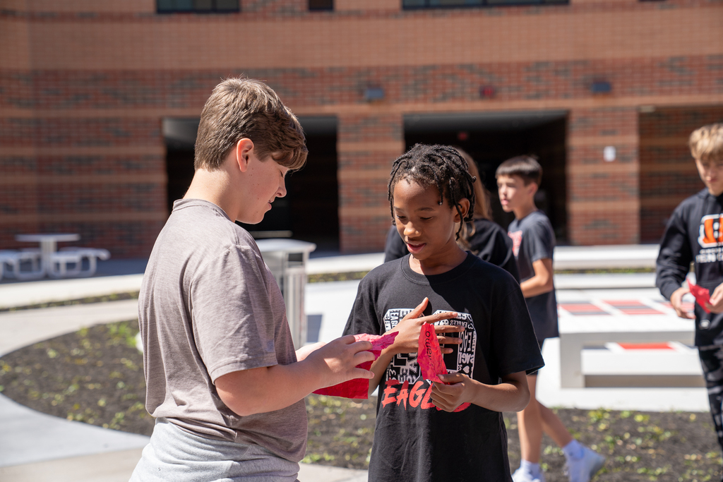 Two male students holding red pieces of paper, conversing