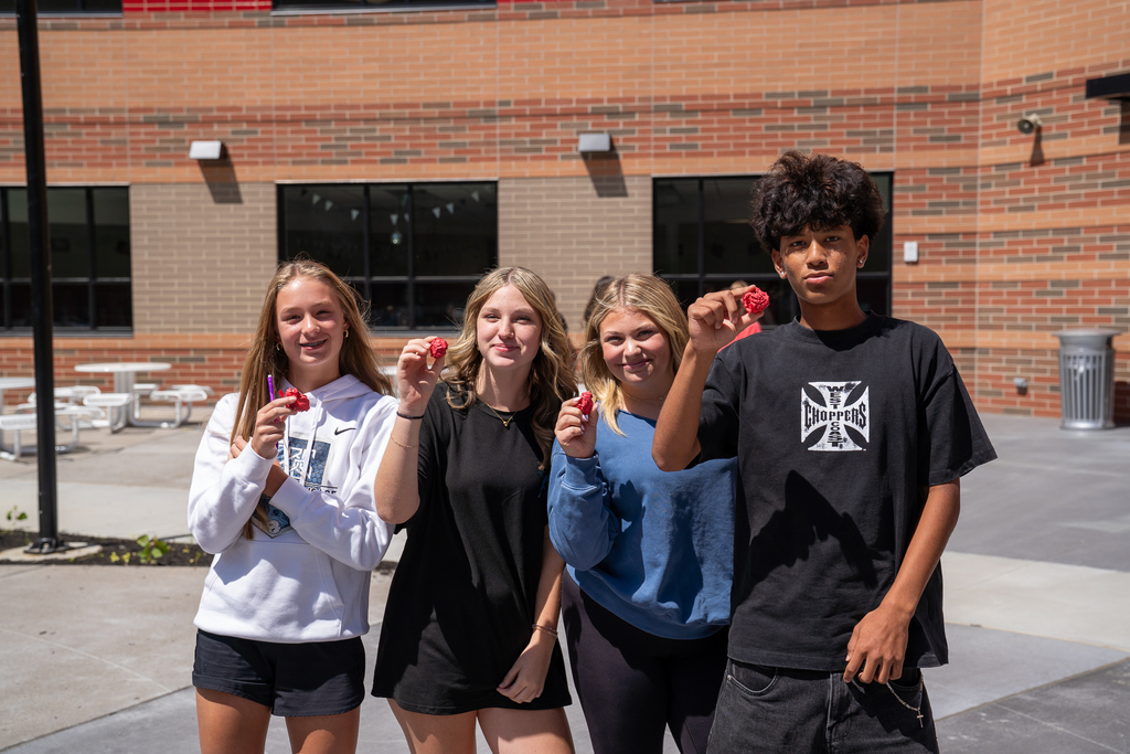 three female blonde students next to male student in black t-shirt. All are holding crumbled red pieces of paper