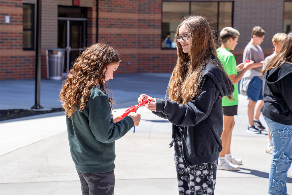 Two students having a conversation and smiling while looking at their red pieces of paper