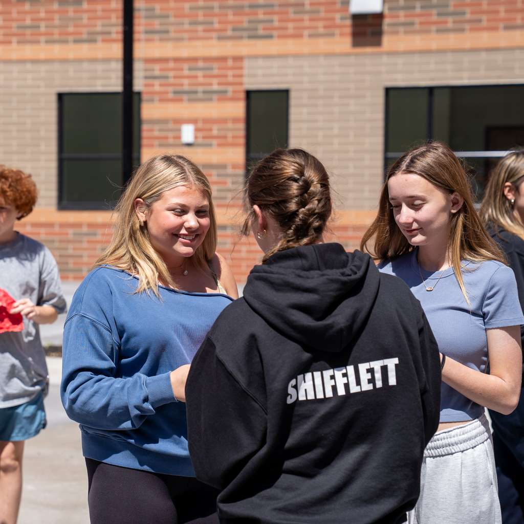 Student with blonde hair smiling at another female student wearing a black hoodie that says "shifflett" 