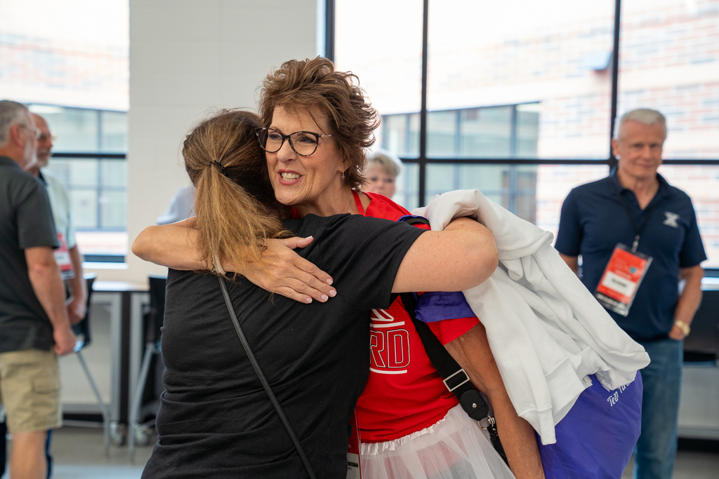 Woman wearing a white tutu and glasses giving a blonde haired woman a hug