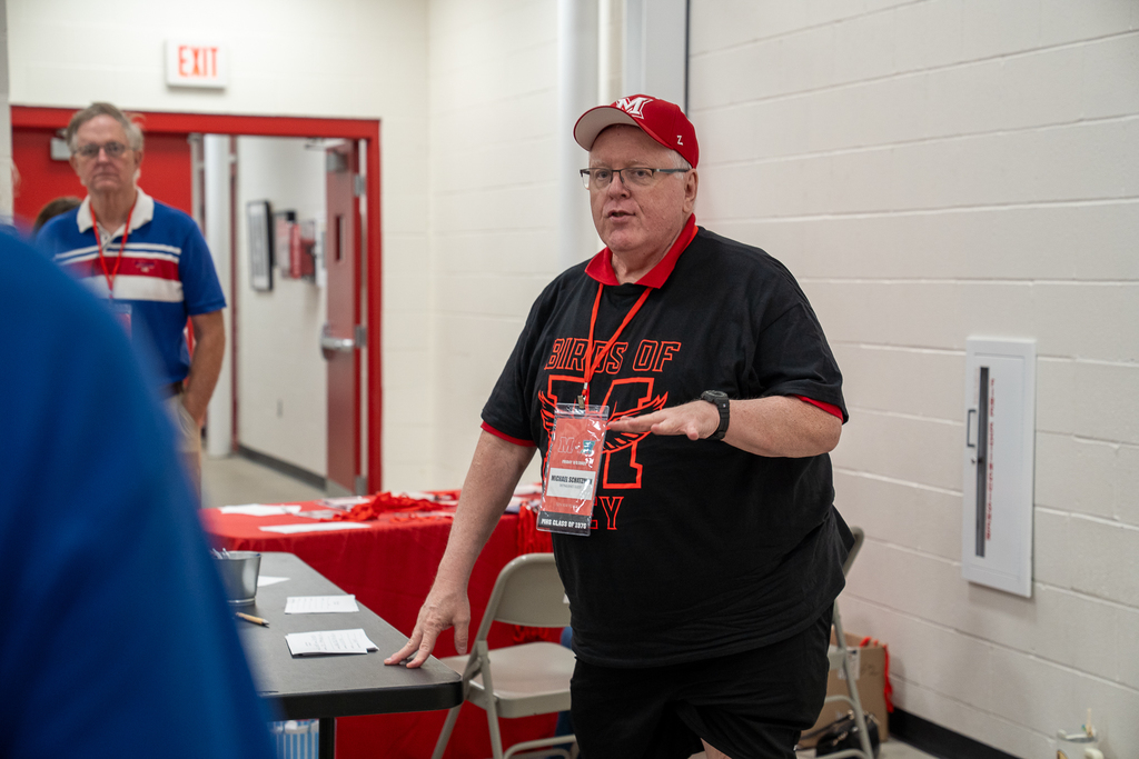 A man in a milford shirt and hat standing to talk
