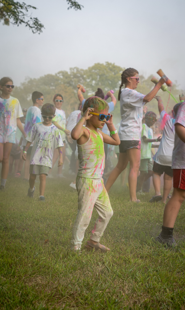 A student adjusting thier sunglasses with dyed blonde hair with paint all over them