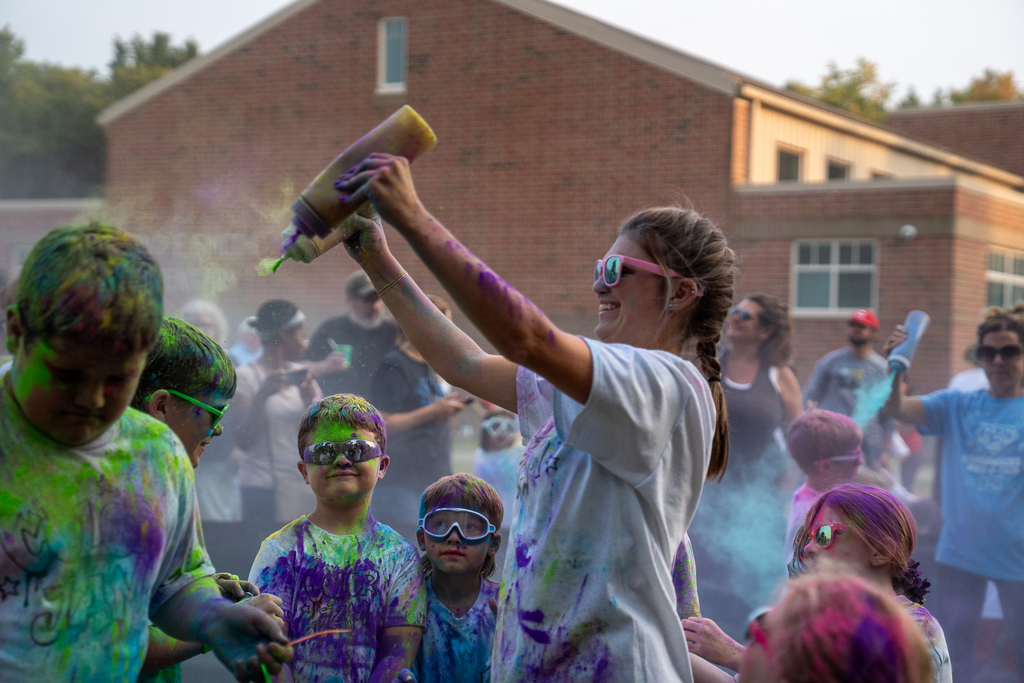 A taller woman with sunglasses on spraying paint on students with two bottles