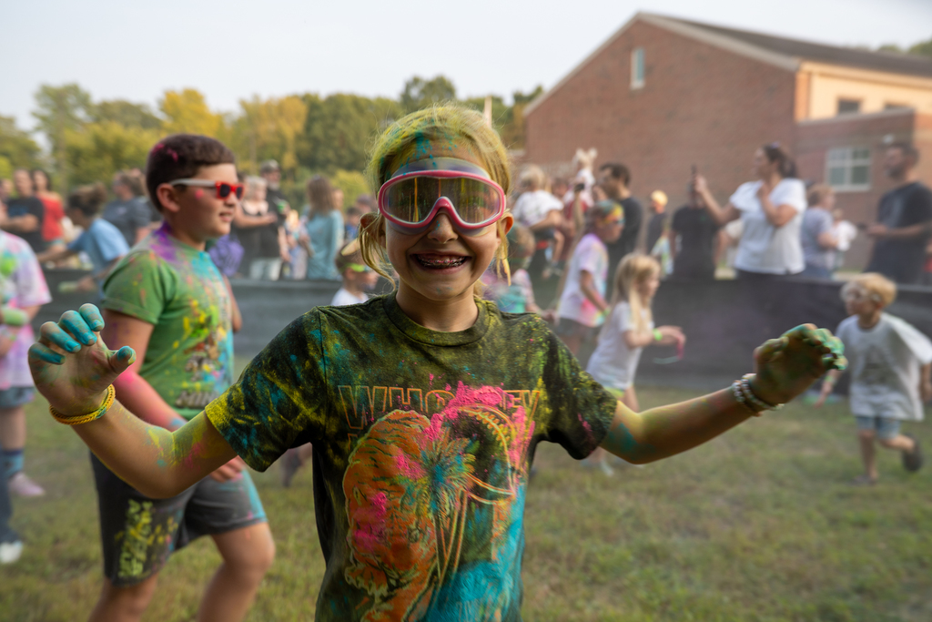 A girl in a who dey shirt covered in paints with goggles on