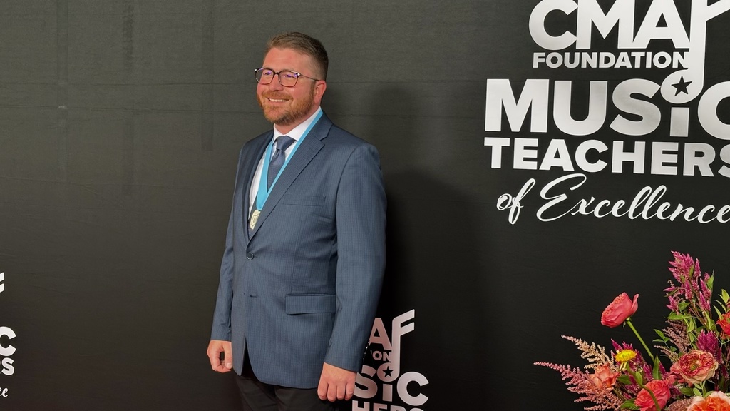 A man in a blue suit and glasses in front of a black banner