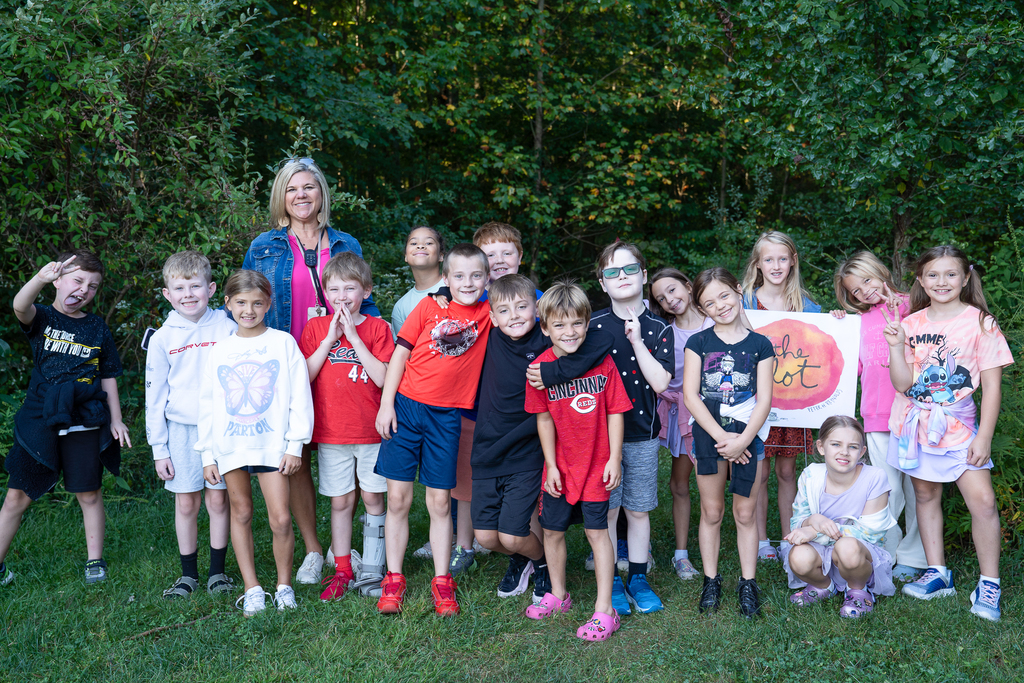 Group photo of students in front of the woods standing on a patch of grass. 