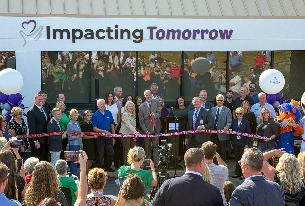 A large ribbon cutting ceremony in front of a building called "IMpacting Tomorrow" 