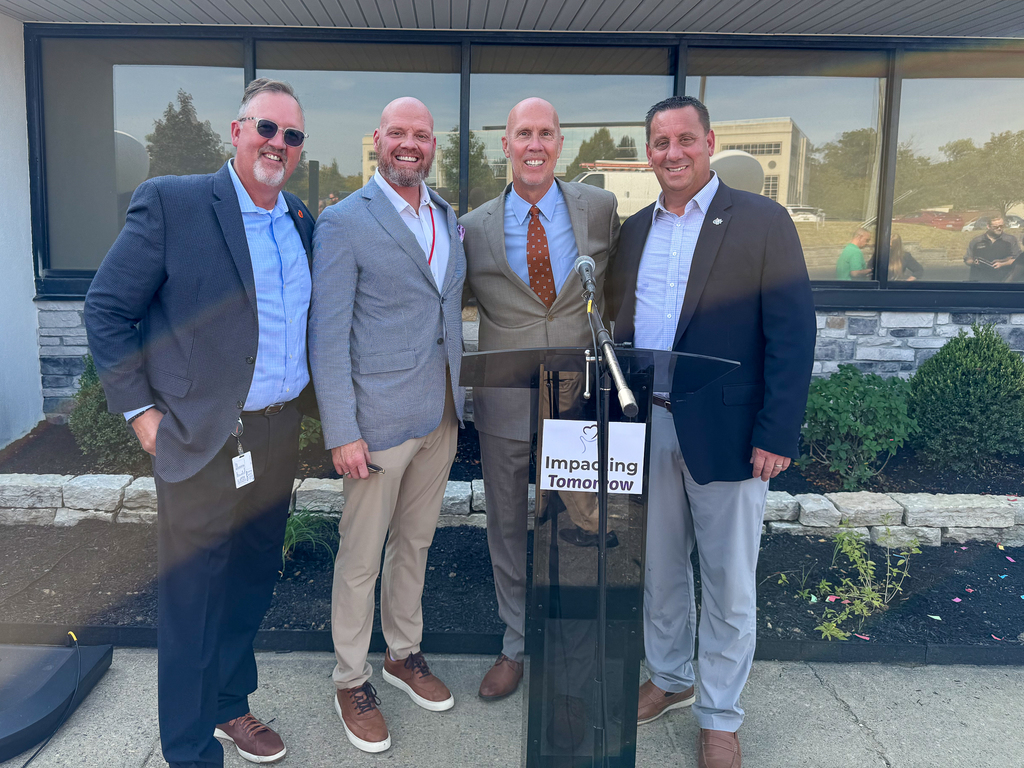 A group of 4 men in front of an "Impacting Tomorrow" podium