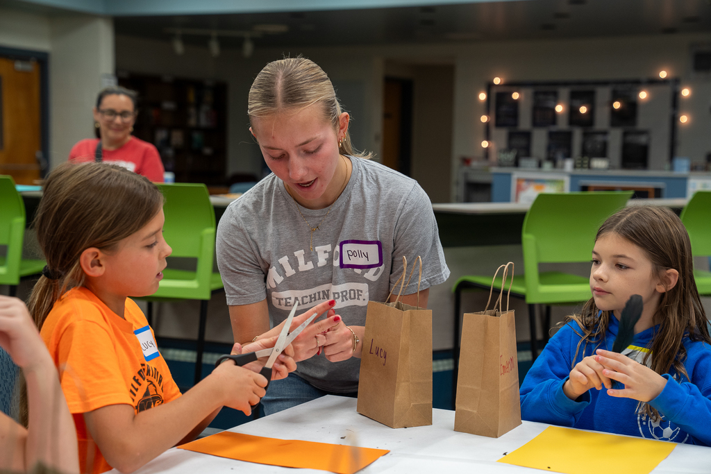 A woman with a ponytail helping a kid with scissors