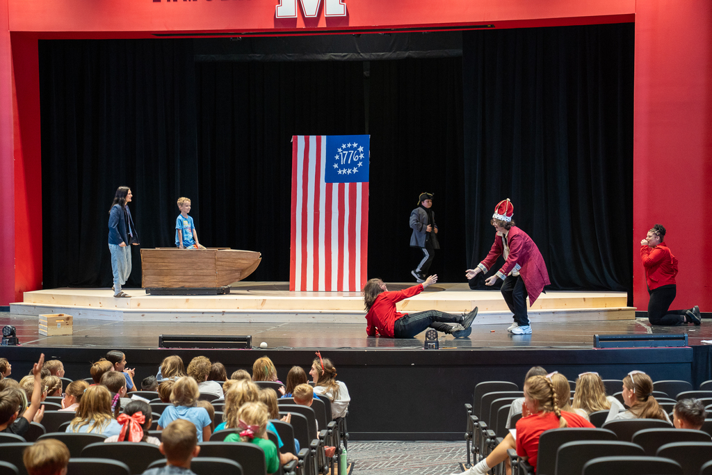 A stage with a large american flag and a prop boat with kids