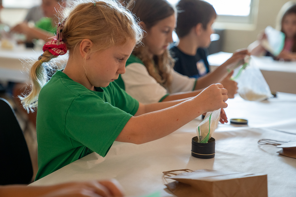 A girl with a ponytail and green shirt making a candle 