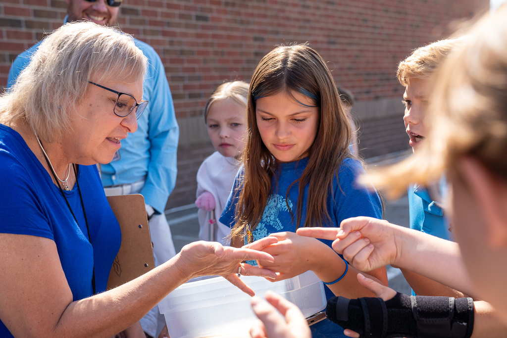 A woman with glasses holding a butterfly while a girl and other hold out their hands