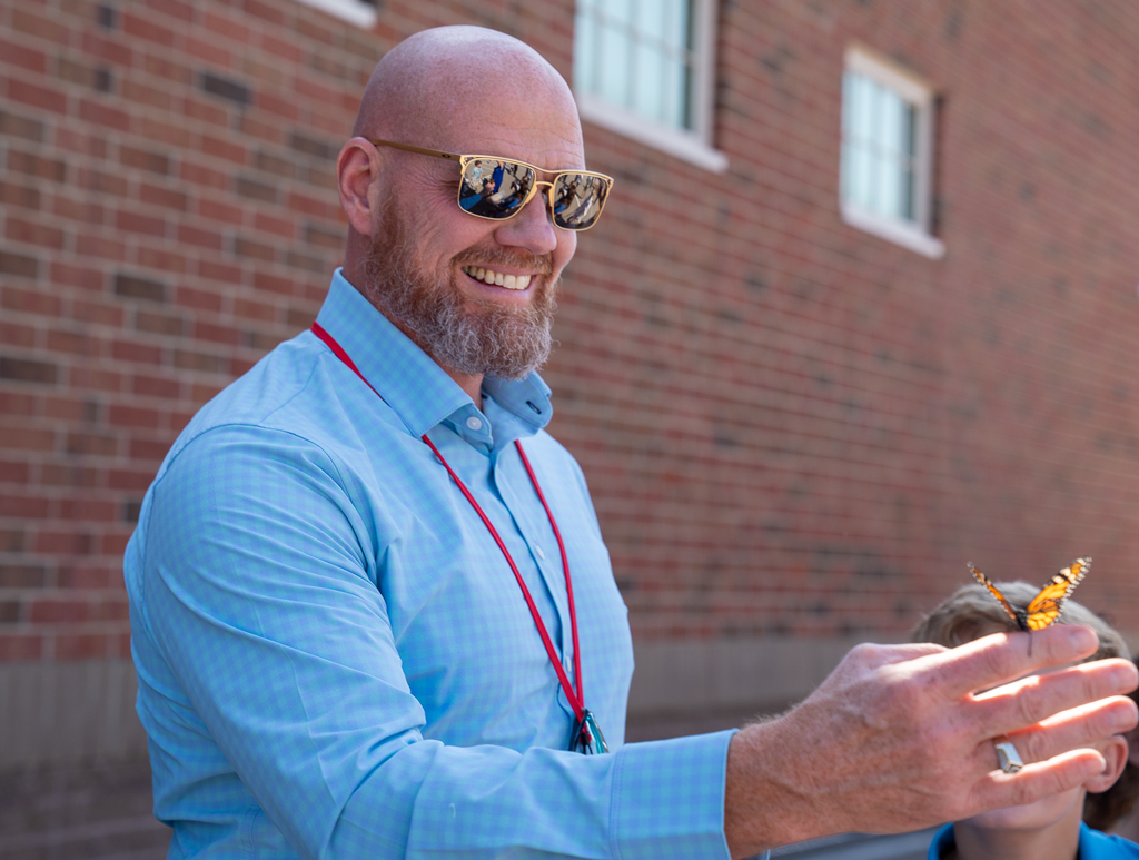 A bald man with sunglasses holding a butterfly