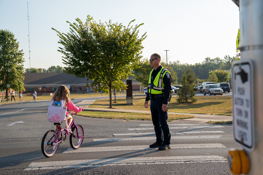 A girl on a pink bicycle stolling past a man in a police officer's uniform manning a sidewalk
